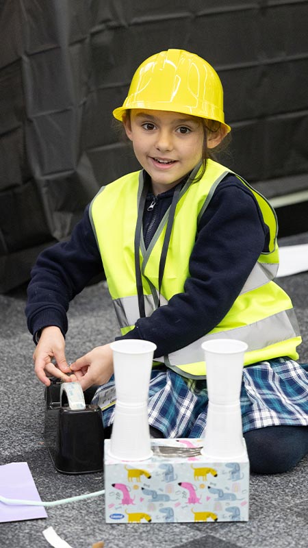 Holy Family Primary Emerton student wearing hard hat. She is constructing a model nuculear power plant.