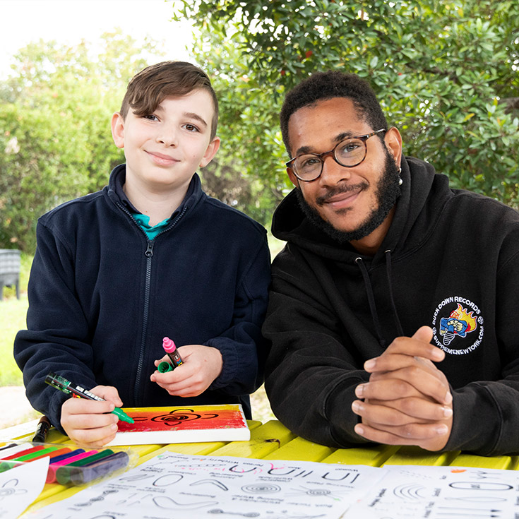 Student and teacher at Holy Family Primary Emerton. The teacher is assisting the student paint Aboriginal art