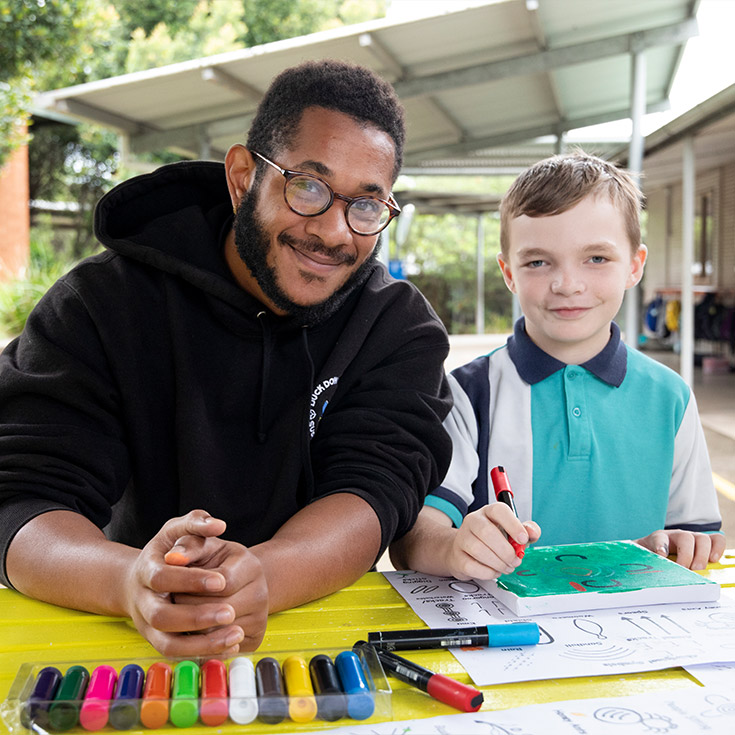 Teacher assisting Holy Family Primary, Emerton students with painting Aboriginal Artwork